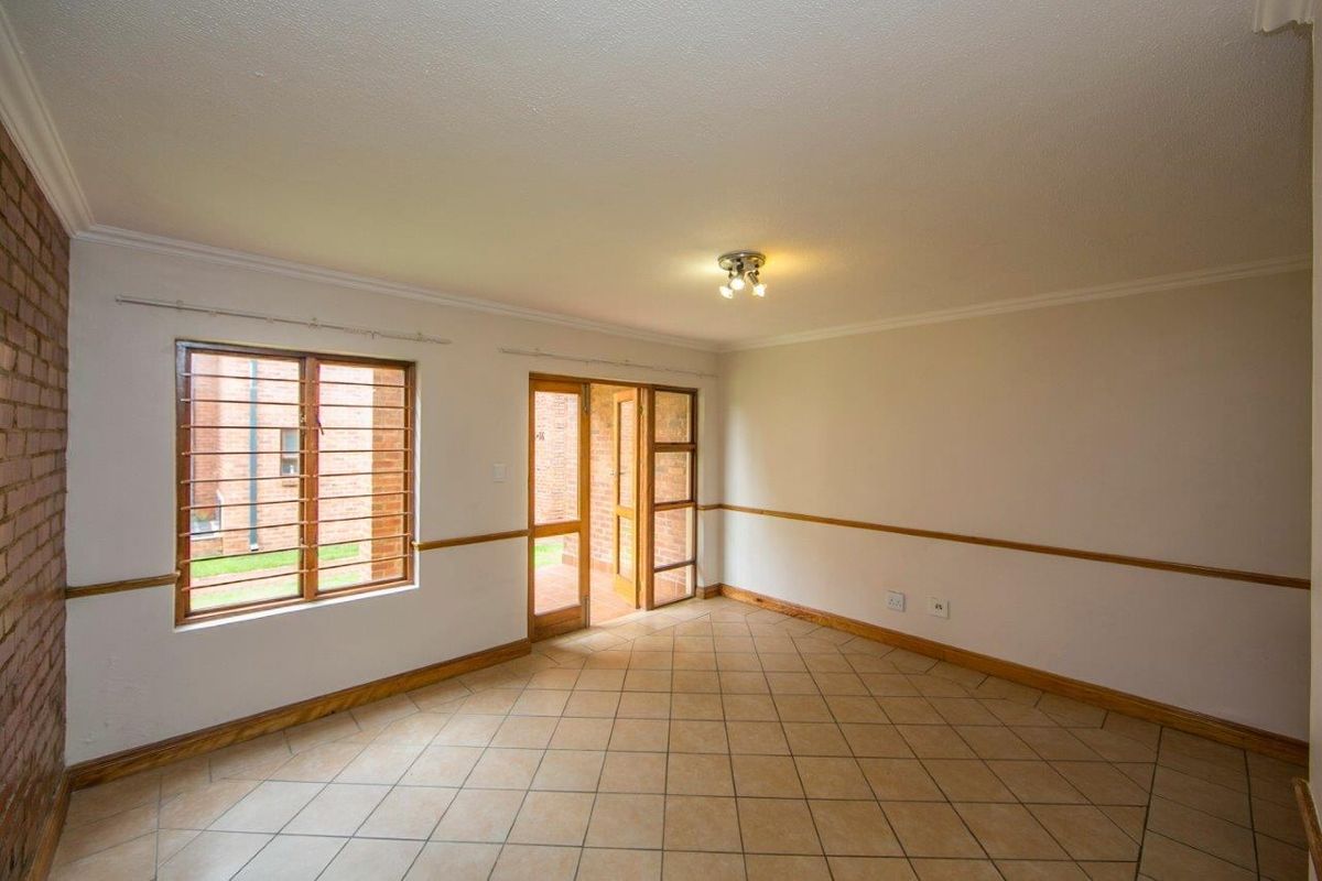 An empty living room featuring tiled flooring, timber window and door frames with security bars, and decorative chair rail molding.