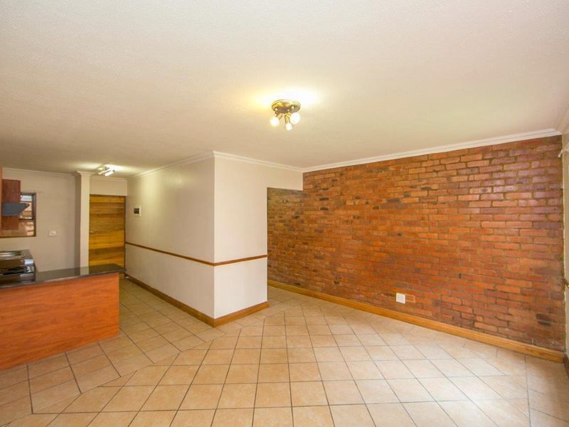 An open-plan living and kitchen area featuring ceramic floor tiles, an exposed brick feature wall, and a functional kitchen with granite countertops.