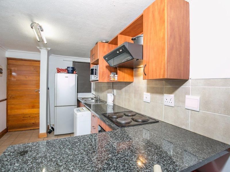 A functional kitchen featuring granite countertops, wooden cabinetry, an electric hob with extractor fan, and tiled backsplash.