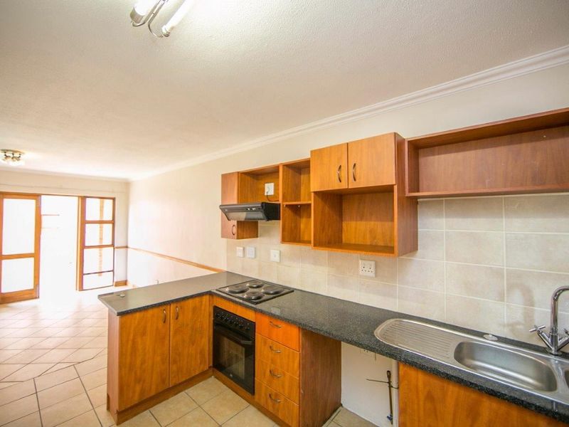 Open plan kitchen featuring wooden cabinetry, granite countertops, and tiled flooring, flowing into a living area with access to a patio or balcony.