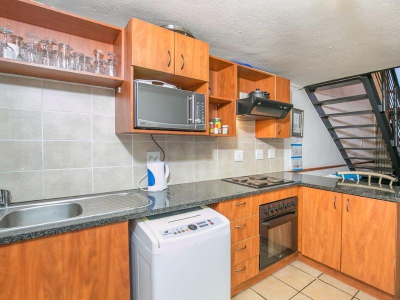 Compact kitchen featuring laminate cabinetry, granite countertops, built-in oven with hob, and tiled backsplash, conveniently located adjacent to the staircase.