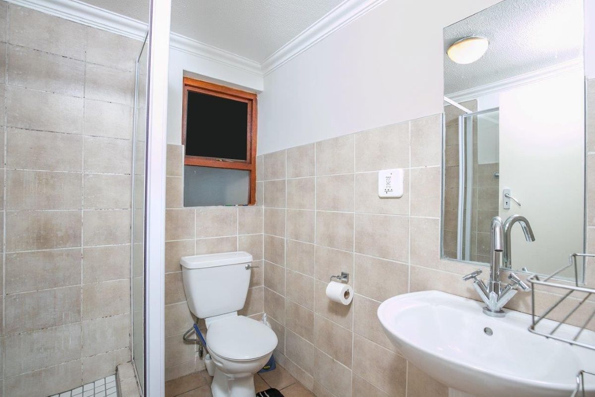 A functional bathroom featuring a pedestal basin, toilet, and a glass-enclosed shower with neutral wall and floor tiling.