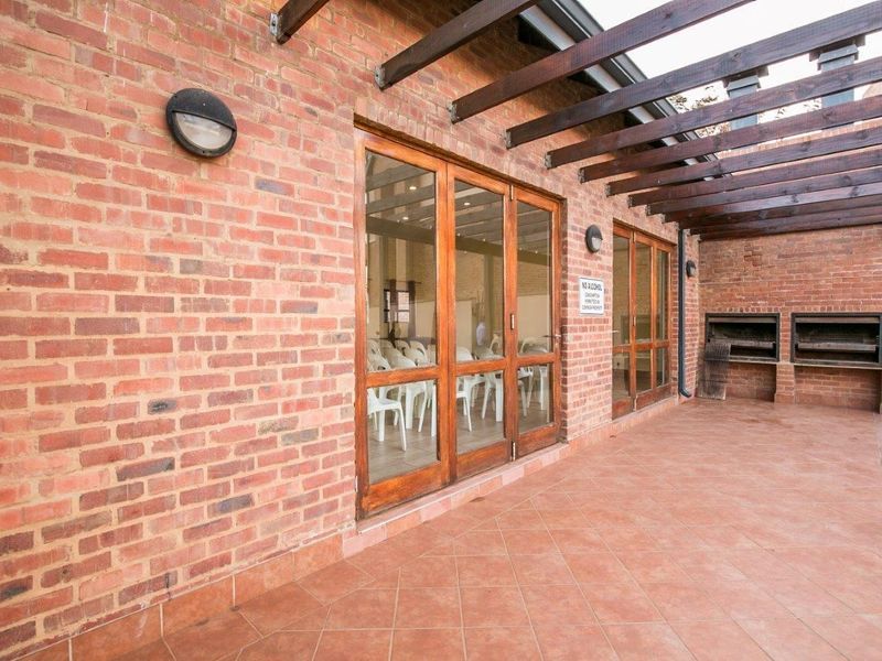 A covered patio area featuring exposed brick walls, a timber pergola, and a built-in brick braai, providing a functional outdoor entertainment space.