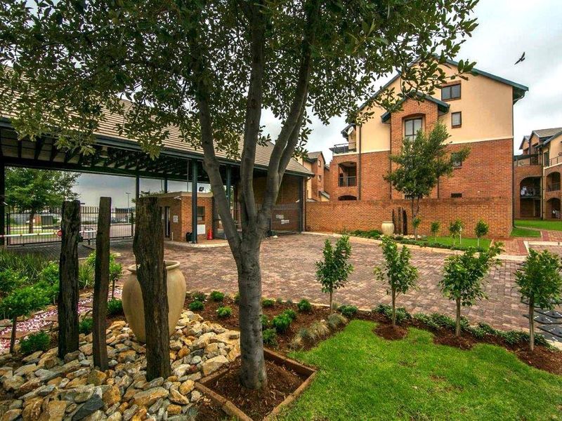 A well-maintained apartment complex entrance featuring brick paving, landscaped gardens, and a secure gated access point.
