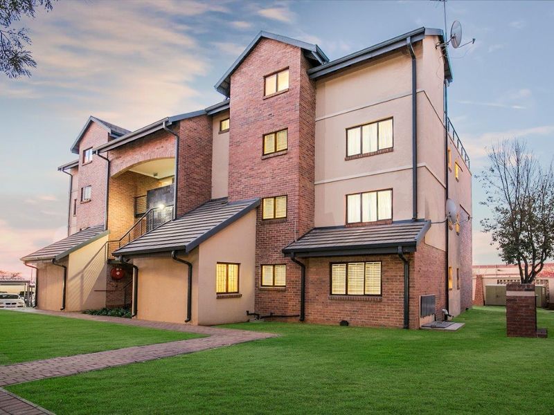 A well-maintained multi-story apartment building featuring a combination of brick and rendered facade, tiled roofing, and landscaped grounds with a paved walkway.