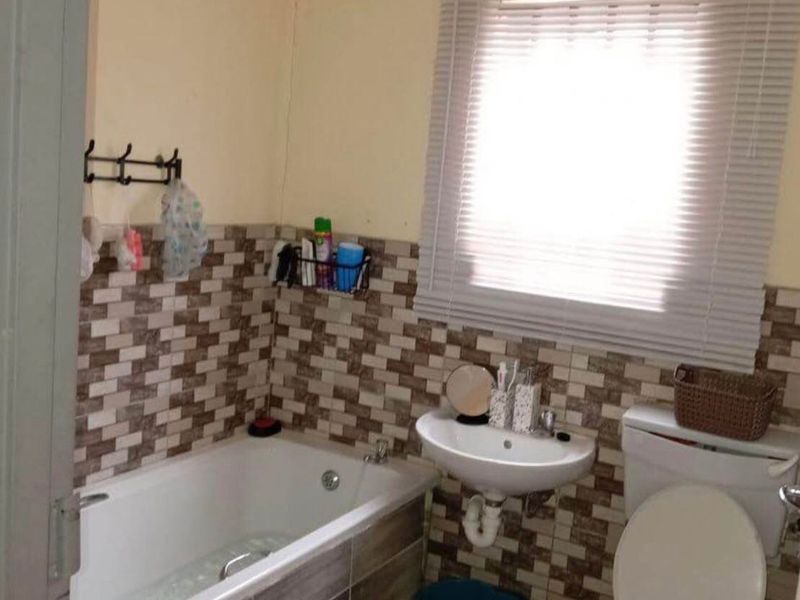 A functional bathroom featuring a bathtub, wall-mounted basin, and toilet with tiled splashbacks and a window blind.