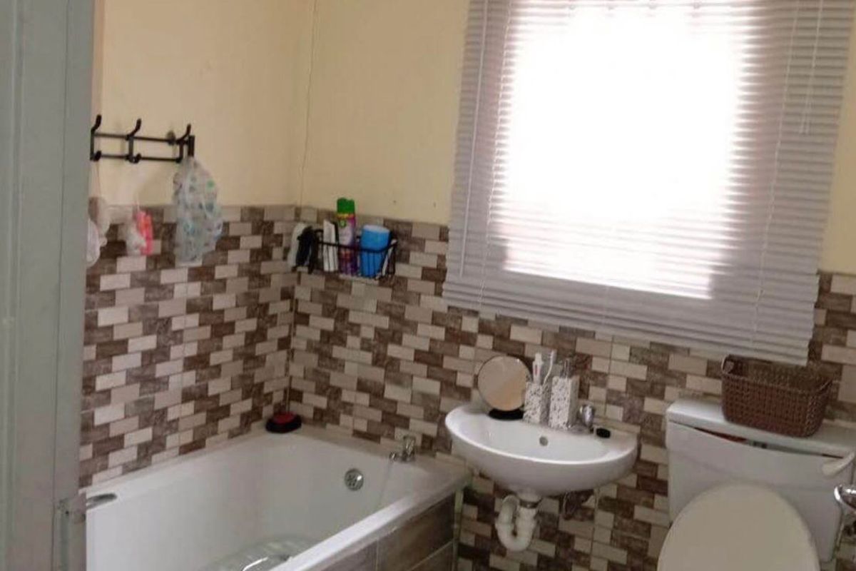 A functional bathroom featuring a bathtub, wall-mounted basin, and toilet with tiled splashbacks and a window blind.