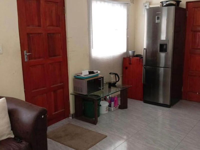 A living area featuring tiled flooring, timber doors, and a window, currently showing signs of wear and dated finishes.
