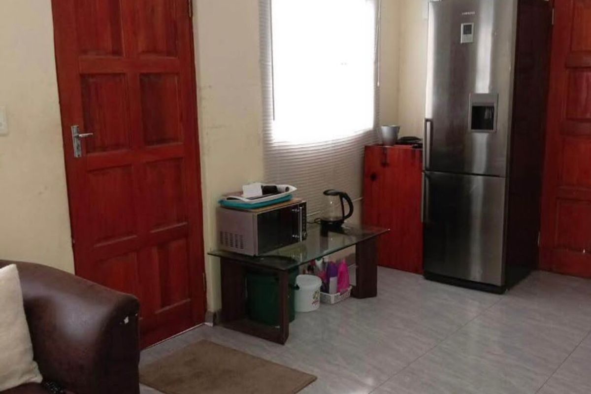 A living area featuring tiled flooring, timber doors, and a window, currently showing signs of wear and dated finishes.