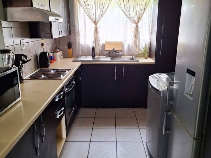 A functional galley-style kitchen featuring dark cabinetry, laminate countertops, built-in electric hob and oven, and tiled flooring with natural light from the window.