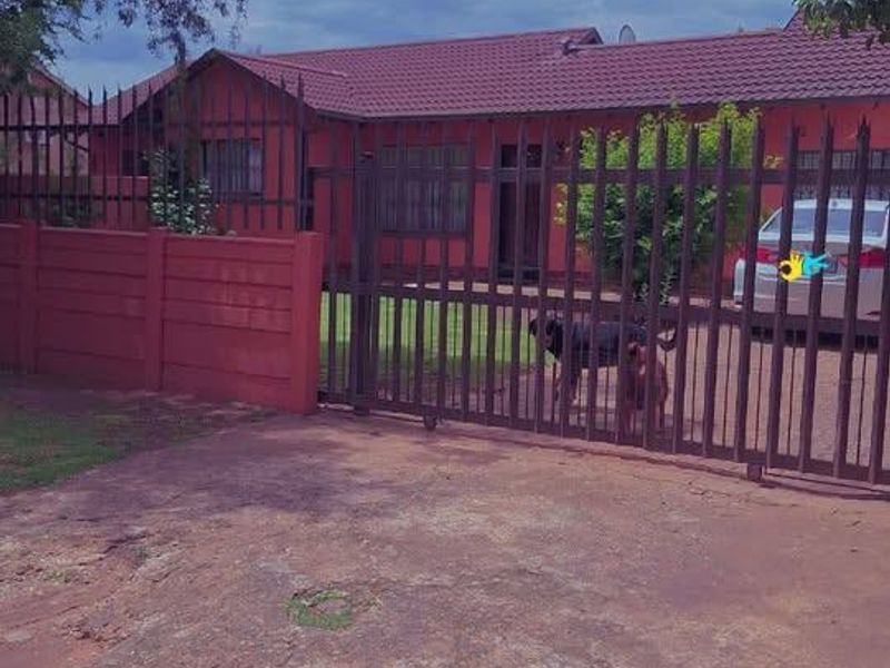 Front view of a single-story house featuring a tiled roof, enclosed by a metal security gate and precast concrete boundary wall.