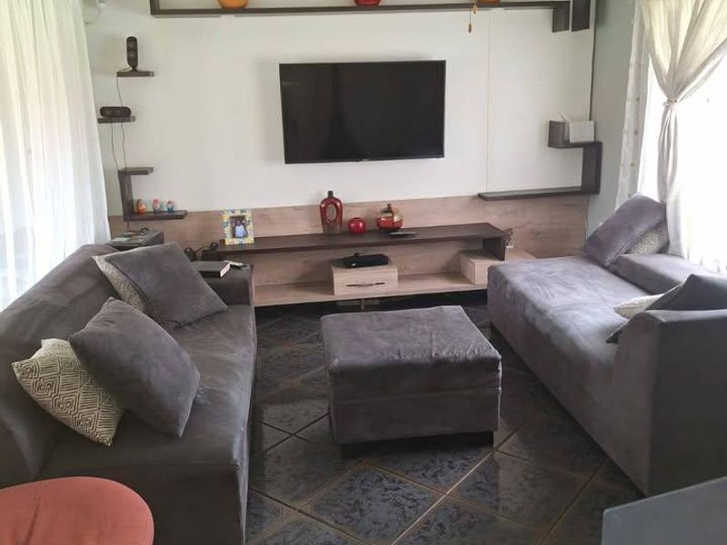 A living room featuring a built-in media wall with shelving, a ceiling fan, and dark tiled flooring.