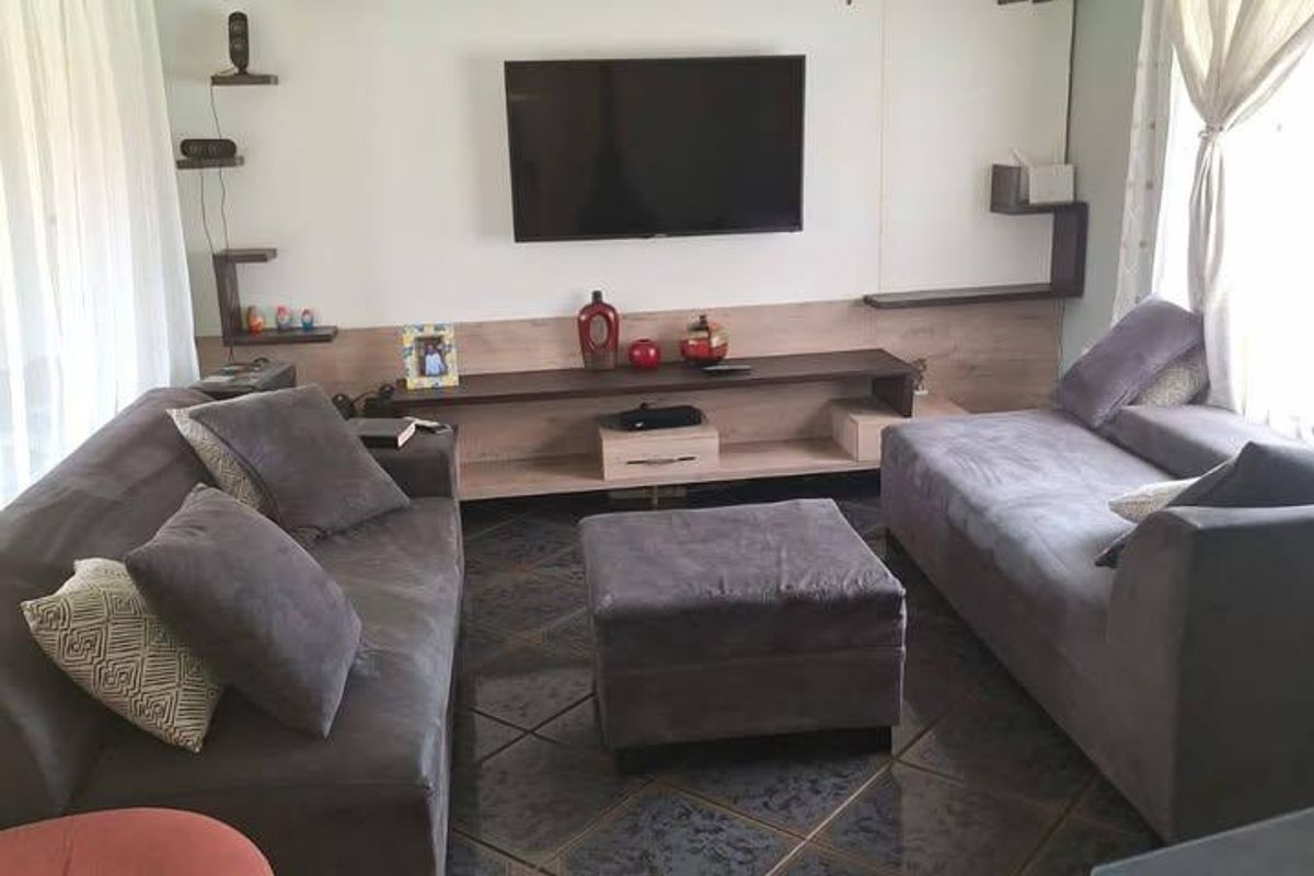 A living room featuring a built-in media wall with shelving, a ceiling fan, and dark tiled flooring.