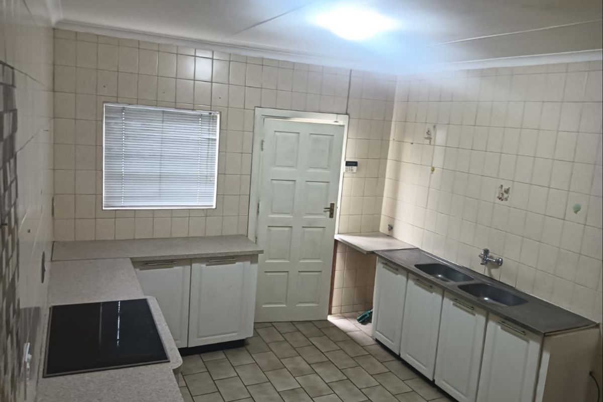 A functional kitchen featuring built-in cabinetry, laminate countertops, a double basin sink, and an electric hob, finished with ceramic wall and floor tiles.