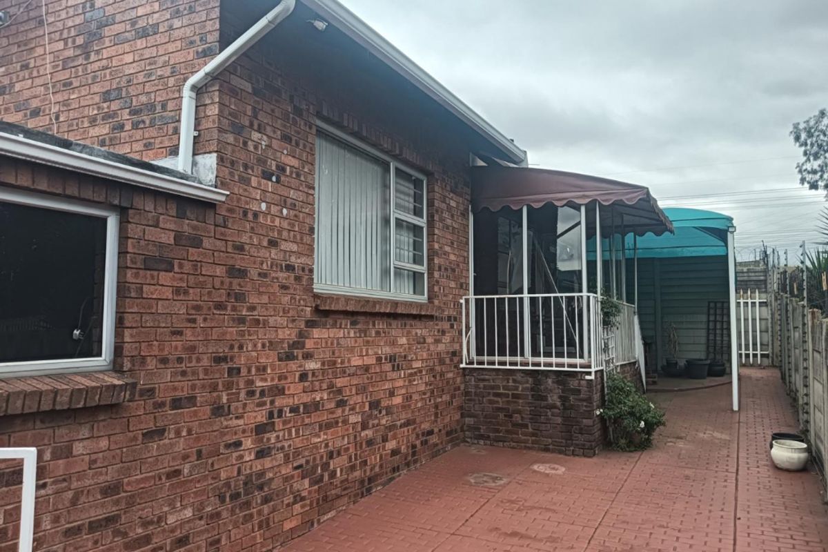 Rear exterior view of the townhouse featuring a face brick facade, paved patio area, and a covered patio with metal awning.