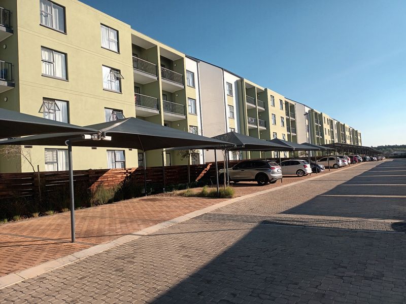 Exterior view of a modern apartment complex featuring paved parking areas with shade cloth carports and private balconies.