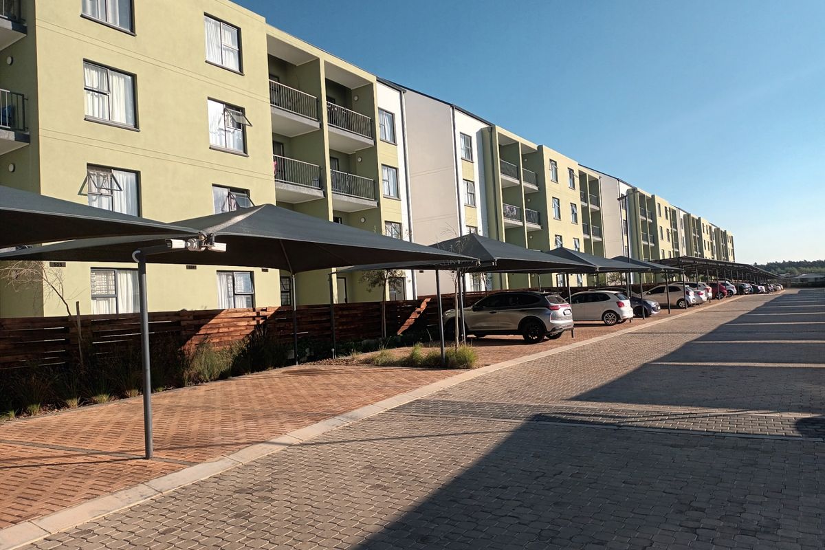 Exterior view of a modern apartment complex featuring paved parking areas with shade cloth carports and private balconies.