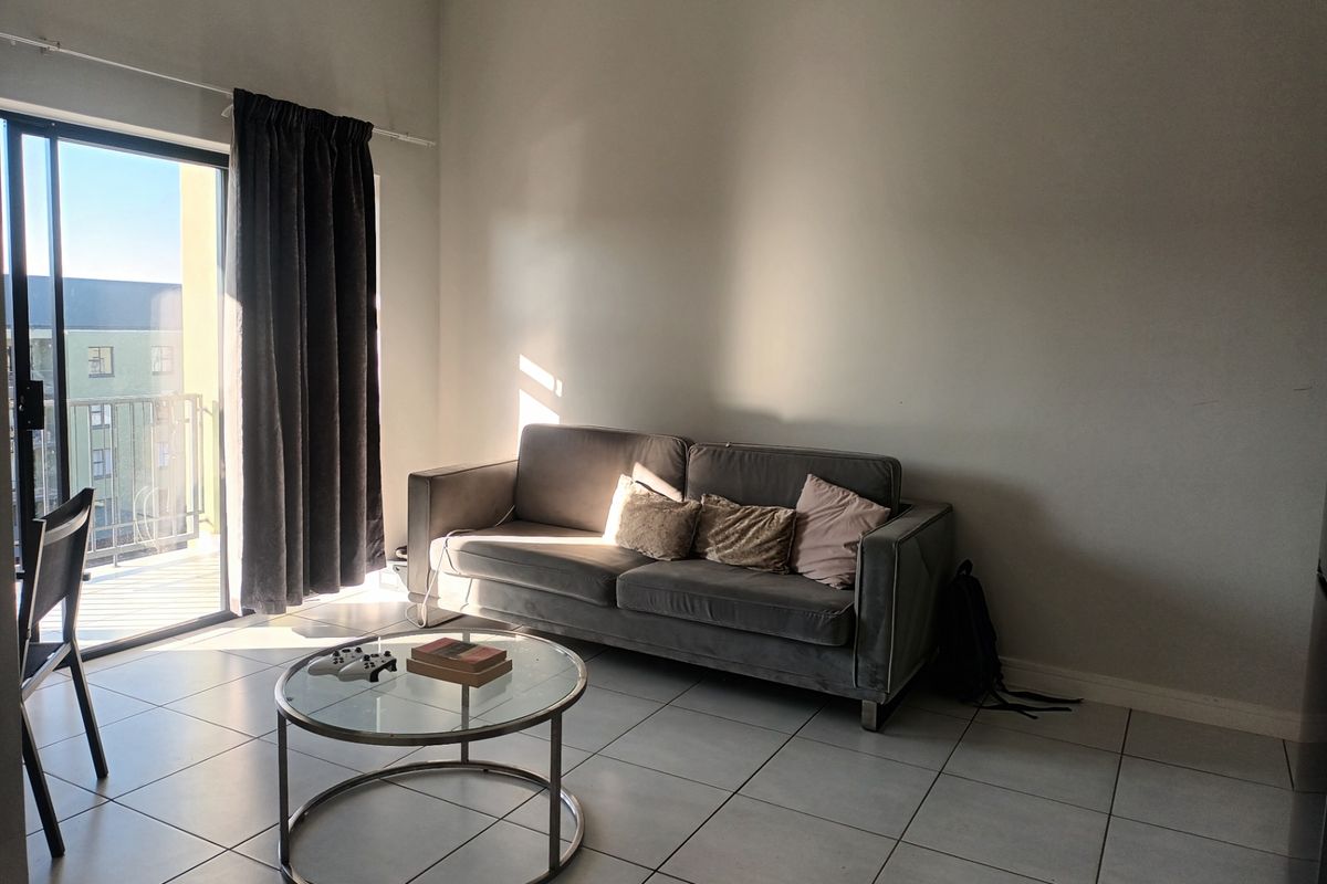 A living room area featuring tiled flooring and a large sliding glass door providing access to an outdoor balcony.