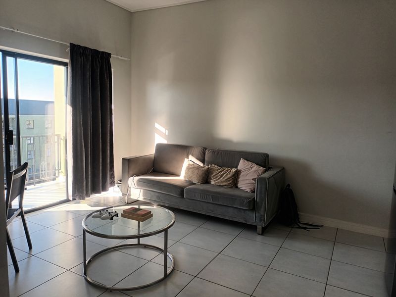 A living room area featuring tiled flooring and a large sliding glass door providing access to an outdoor balcony.