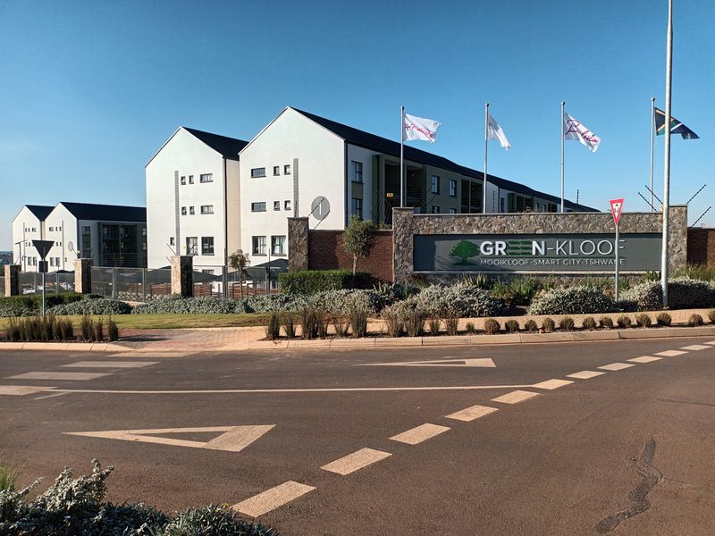 Street view of the Green-Kloof apartment complex entrance, featuring modern multi-story residential buildings, stone-clad signage, and well-maintained landscaped grounds.