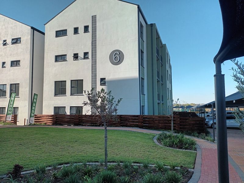 Exterior view of a modern apartment building featuring landscaped gardens, paved walkways, and dedicated covered parking facilities.