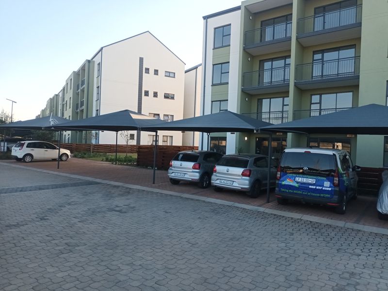 Exterior view of a modern apartment complex featuring paved parking areas with shade cloth carports and multi-story residential units with balconies.