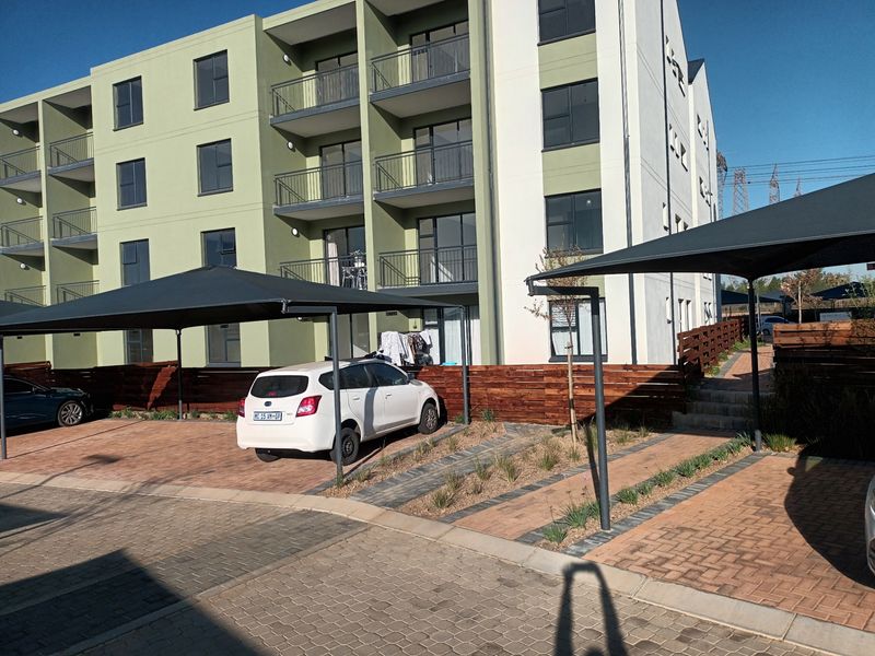 Exterior view of a modern apartment complex featuring paved parking areas with shade cloth carports, timber fencing, and private balconies.