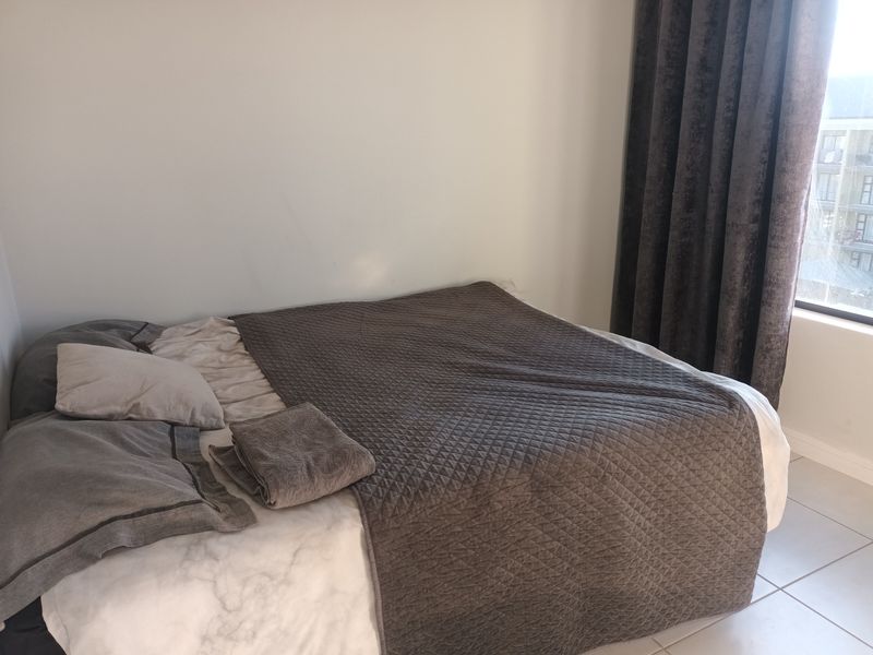 A bedroom featuring neutral wall finishes and tiled flooring, with natural light provided by a window dressed with floor-to-ceiling curtains.