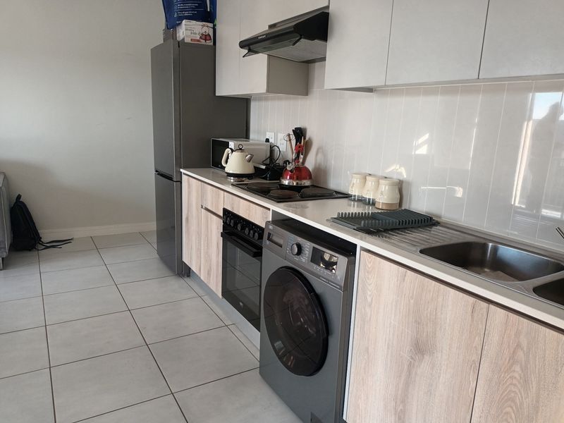 Modern kitchen featuring light wood-grain cabinetry, white tiled backsplash, integrated electric hob, oven, and extractor fan with neutral floor tiles.