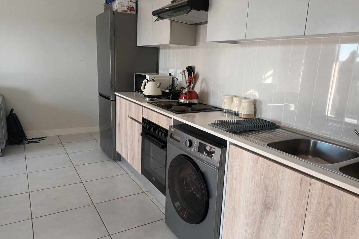 Modern kitchen featuring light wood-grain cabinetry, white tiled backsplash, integrated electric hob, oven, and extractor fan with neutral floor tiles.