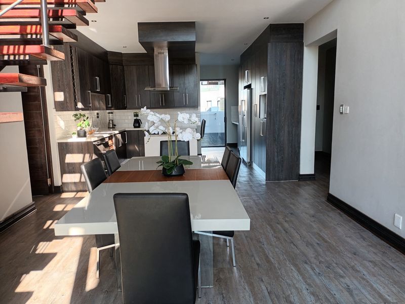 Modern open-plan kitchen and dining area featuring dark wood cabinetry, stainless steel extractor fan, subway tile backsplash, and a striking floating staircase.