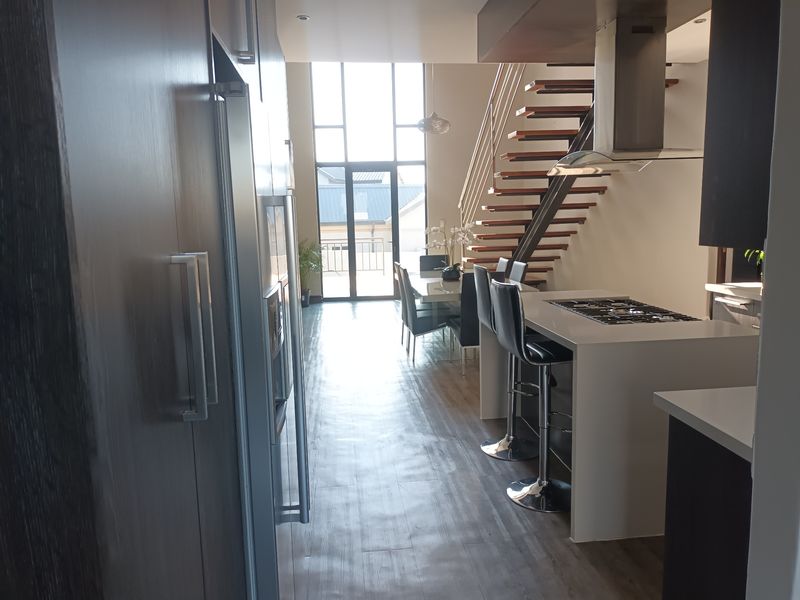 Modern open-plan kitchen and living area featuring a central island with gas cooktop, sleek cabinetry, and a striking floating staircase leading to upper levels.