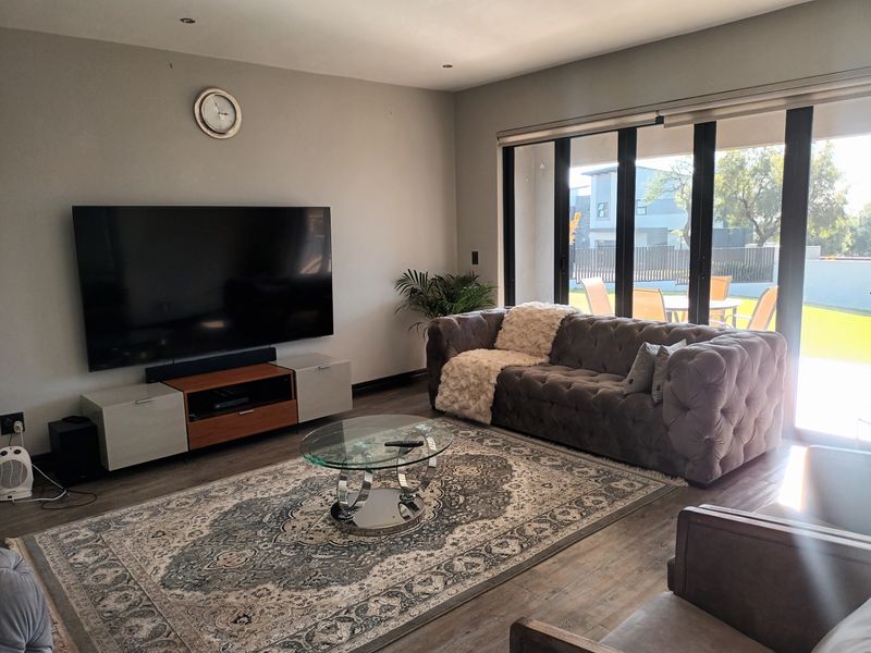 A modern living room featuring laminate flooring, recessed lighting, and large bi-fold glass doors that provide seamless access to the outdoor patio area.