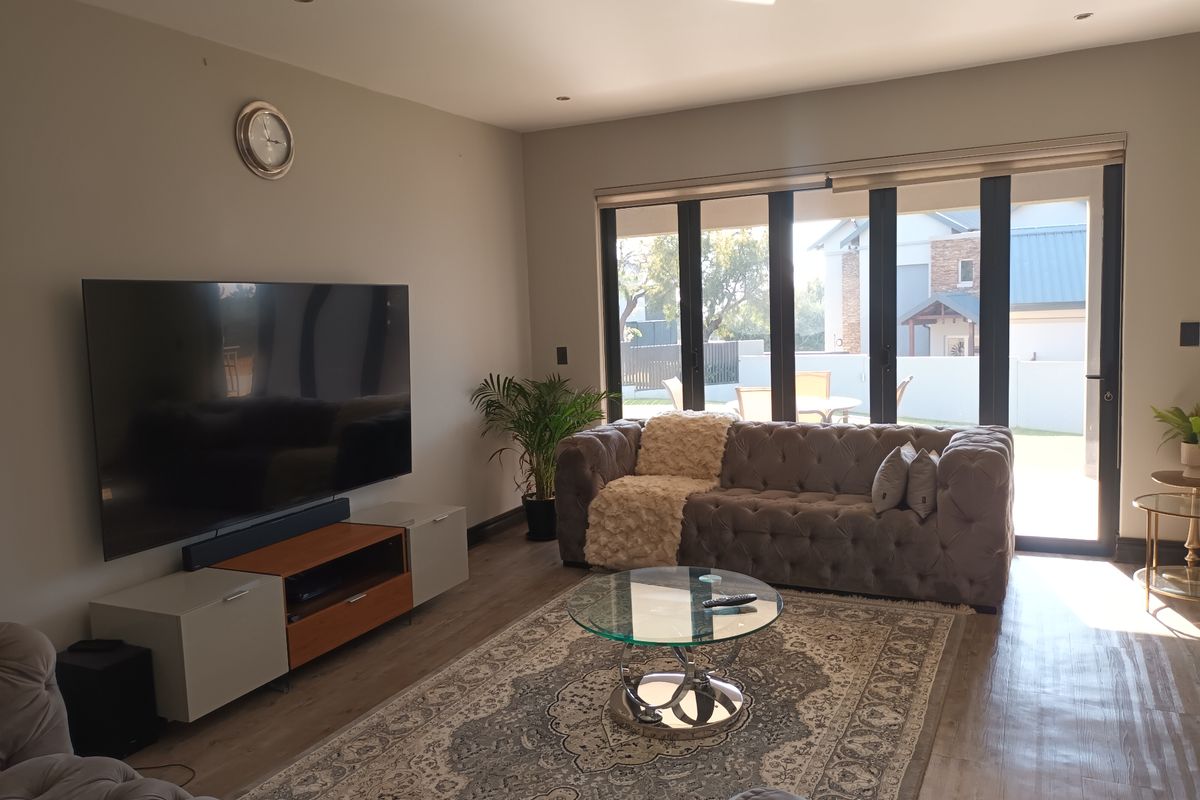 A well-maintained living room featuring modern laminate flooring, recessed lighting, and large black aluminium stacker doors that provide seamless access to the outdoor area.