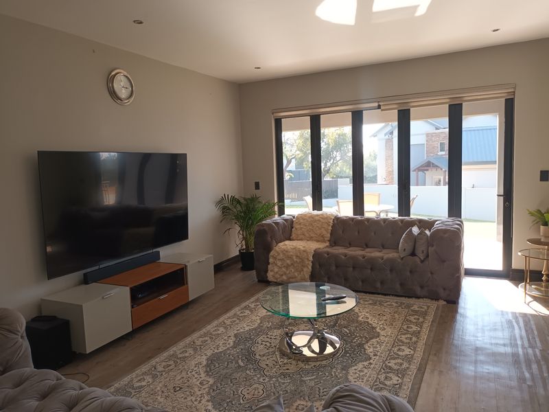 A well-maintained living room featuring modern laminate flooring, recessed lighting, and large black aluminium stacker doors that provide seamless access to the outdoor area.