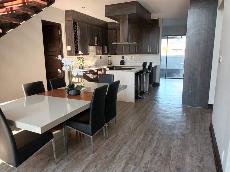 Modern open-plan kitchen and dining area featuring dark wood cabinetry, a central island with breakfast bar, and durable laminate flooring.