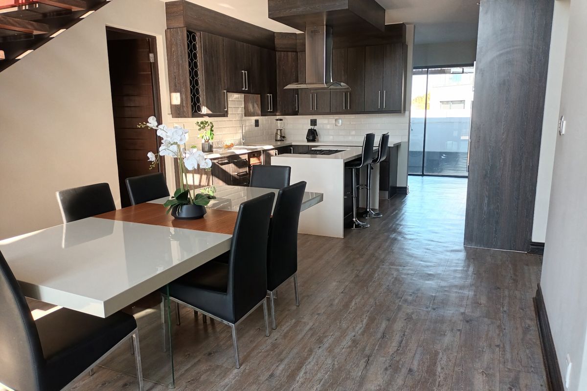 Modern open-plan kitchen and dining area featuring dark wood cabinetry, a central island with breakfast bar, and durable laminate flooring.