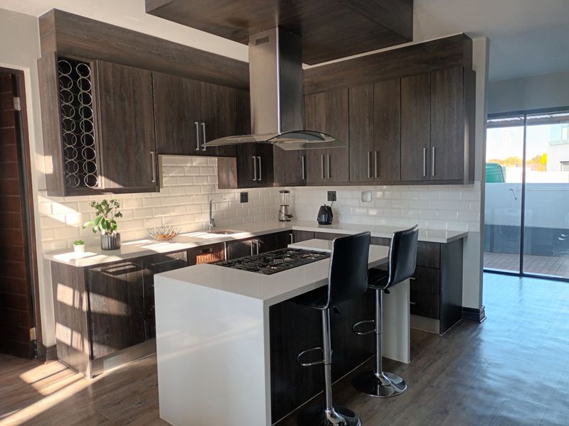 Modern kitchen featuring dark wood cabinetry, white subway tile backsplash, stone countertops, a central island with a gas cooktop, and stainless steel extractor fan.