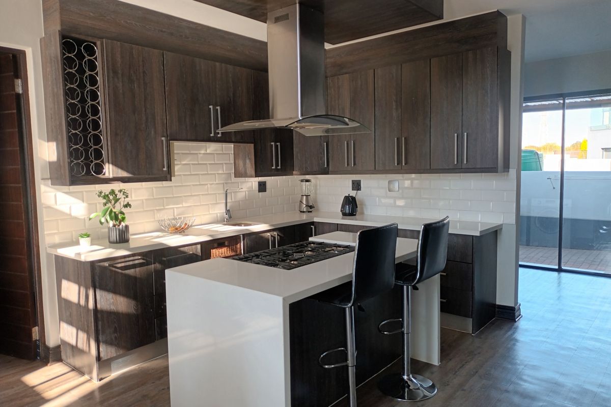 Modern kitchen featuring dark wood cabinetry, white subway tile backsplash, stone countertops, a central island with a gas cooktop, and stainless steel extractor fan.