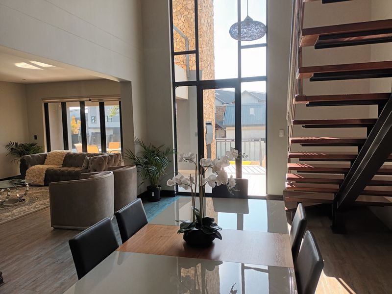 Spacious open-plan living and dining area featuring double-volume ceilings, floor-to-ceiling windows, and a modern floating staircase with timber treads.