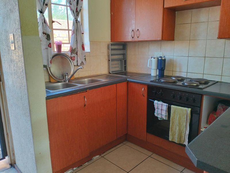 A functional kitchen featuring laminate cabinetry, a double bowl stainless steel sink, tiled backsplash, and a built-in electric oven with hob.
