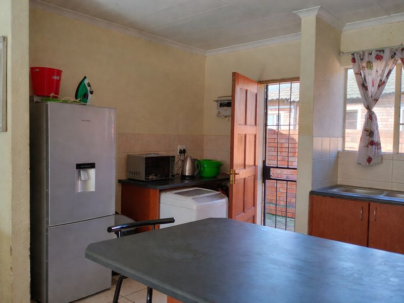 A functional kitchen area featuring laminate countertops, built-in cabinetry, and a double sink, with direct access to an exterior courtyard through a security gate.