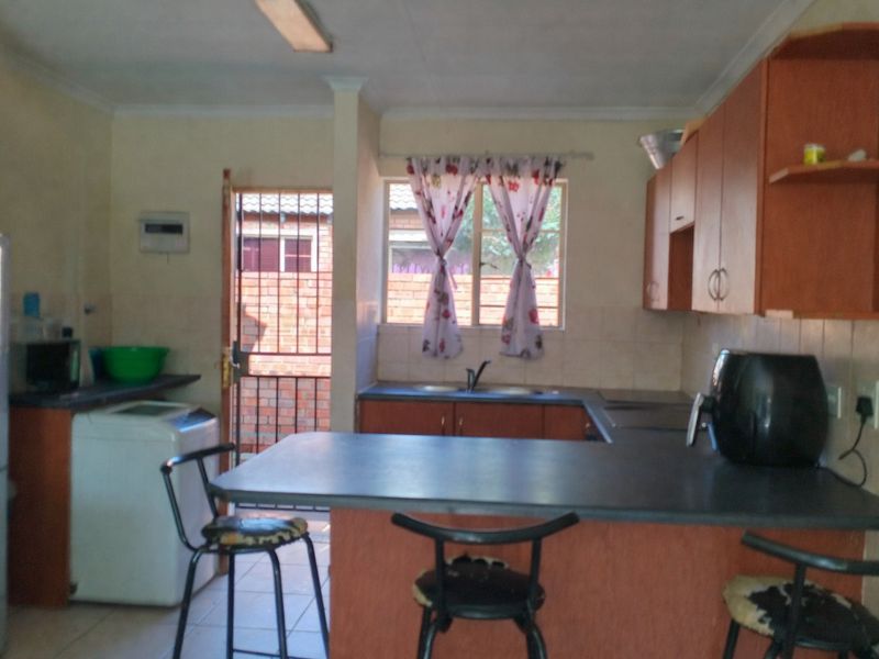 A functional kitchen featuring built-in cabinetry, laminate countertops, and a breakfast nook, with direct access to an exterior security gate.
