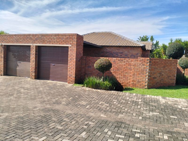 Front view of a townhouse featuring a double garage with roller doors, brick exterior, tiled roof, and a paved driveway.