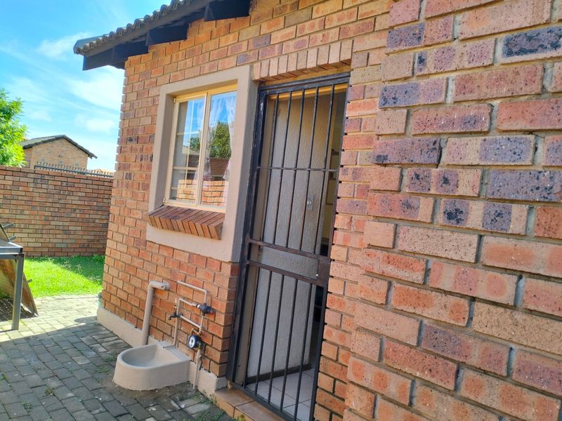 Rear exterior view of the townhouse featuring face brick construction, a security gate, and an external water tap on a paved patio area.