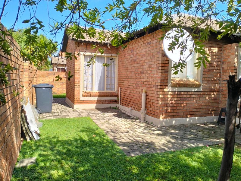 Rear view of the townhouse featuring a face brick exterior, tiled roof, and a private paved patio area with surrounding garden space.