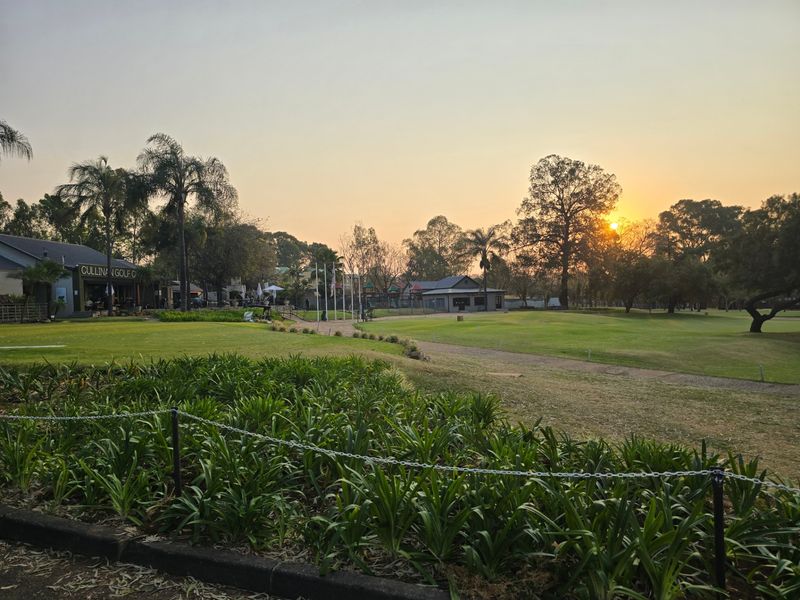 A scenic view of a well-maintained golf course landscape at sunset, featuring lush green lawns and mature trees.