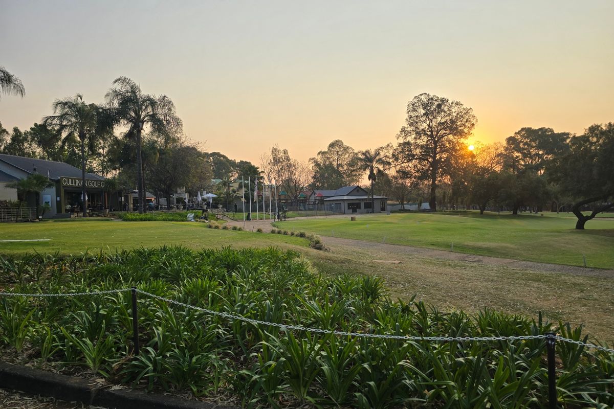A scenic view of a well-maintained golf course landscape at sunset, featuring lush green lawns and mature trees.
