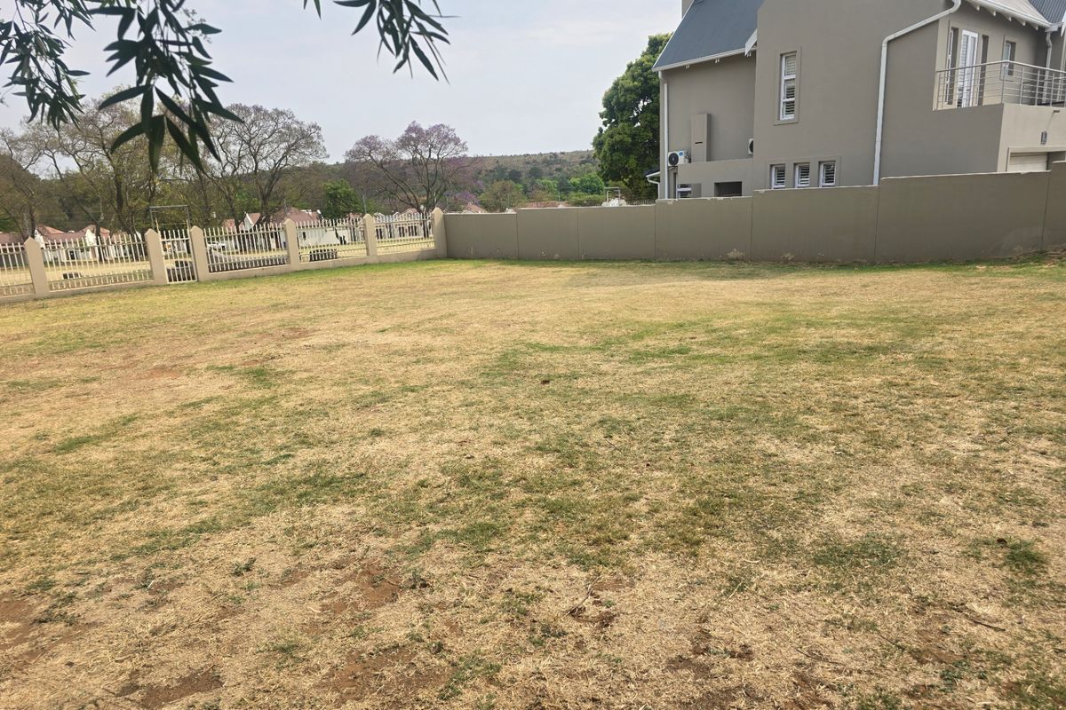 A view of a vacant residential plot featuring a perimeter wall, metal fencing, and established lawn area.