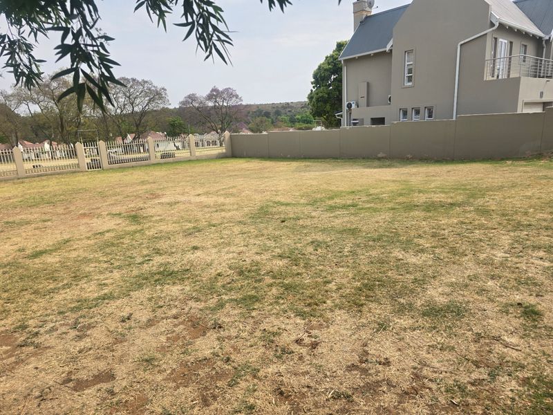 A view of a vacant residential plot featuring a perimeter wall, metal fencing, and established lawn area.